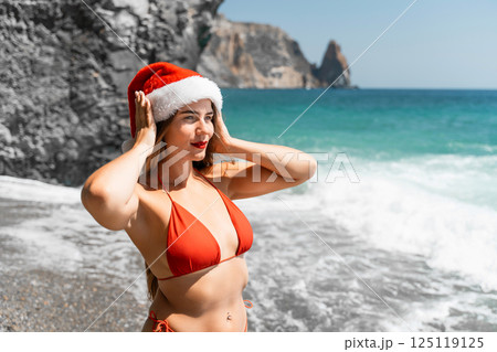 A woman in Santa hat on the seashore, dressed in a red swimsuit. New Year's celebration in a hot country A woman in Santa hat on the seashore, dressed in a red swimsuit. New Year's celebration in a hot country 125119125