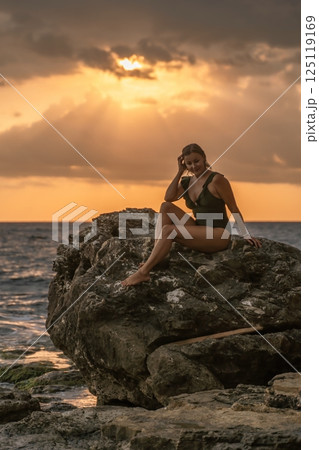 Woman Sunset Beach - Silhouette of woman sitting on a rock at sunset with the ocean behind her. Woman Sunset Beach - Silhouette of woman sitting on a rock at sunset with the ocean behind her. 125119169