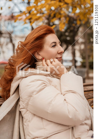 Woman Autumn Park Portrait: Redhead thoughtfully sits outdoors, enjoying fall foliage. Woman Autumn Park Portrait: Redhead thoughtfully sits outdoors, enjoying fall foliage. 125119308
