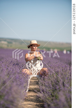 woman sitting in a field of lavender and wearing a straw hat. She is smiling and holding a bouquet of flowers. Scene is peaceful and serene, as the woman is surrounded by the beauty of nature woman sitting in a field of lavender and wearing a straw hat. She is smiling and holding a bouquet of flowers. Scene is peaceful and serene, as the woman is surrounded by the beauty of nature 125119318