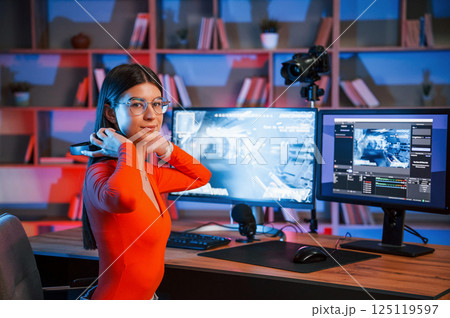 Wearing headphones. Young beautiful game streamer is indoors with pc Wearing headphones. Young beautiful game streamer is indoors with pc 125119597