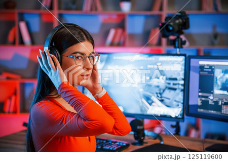 In headphones. Young beautiful game streamer is indoors with pc 125119600
