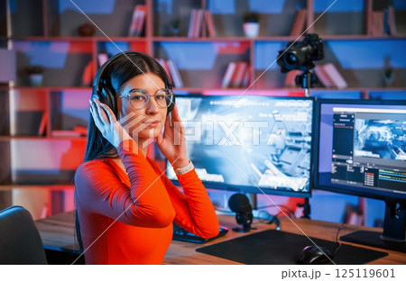 Wearing headphones. Young beautiful game streamer is indoors with pc Wearing headphones. Young beautiful game streamer is indoors with pc 125119601