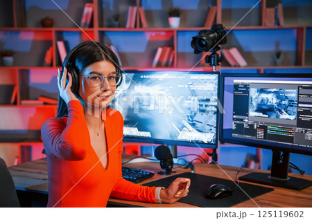 Wearing headphones. Young beautiful game streamer is indoors with pc Wearing headphones. Young beautiful game streamer is indoors with pc 125119602