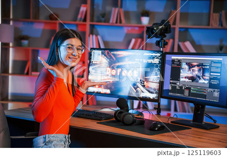 Positive facial expression. Young beautiful game streamer is indoors with pc Positive facial expression. Young beautiful game streamer is indoors with pc 125119603