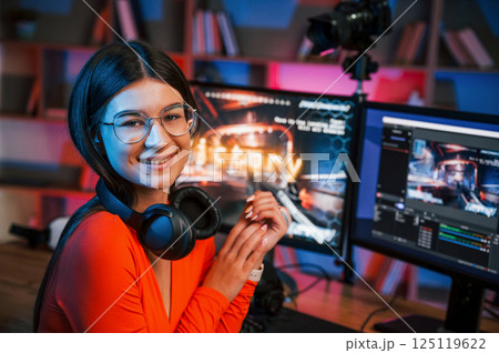 Sitting and smiling. Young beautiful game streamer is indoors with pc Sitting and smiling. Young beautiful game streamer is indoors with pc 125119622
