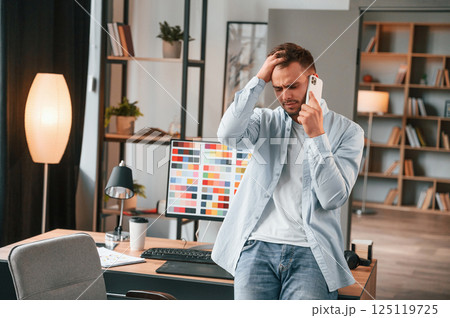 Talking by phone. Young male designer is in the modern office 125119725
