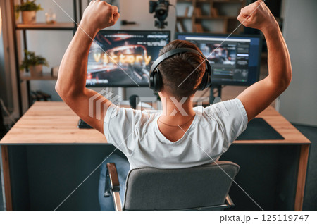 With hands up. Celebrating victory. Young man playing and streaming the first person shooter game With hands up. Celebrating victory. Young man playing and streaming the first person shooter game 125119747