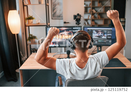 Rear view. Celebrating victory. Young man playing and streaming the first person shooter game 125119752