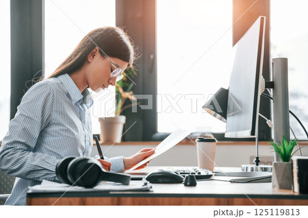 SIde view. Sitting by computer. Young female designer is in the modern office 125119813