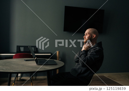 Tired freelancer touching neck while sitting at home office desk with laptop, looking pensive and contemplative after long day of work. Exhausted programmer pondering challenging project. Tired freelancer touching neck while sitting at home office desk with laptop, looking pensive and contemplative after long day of work. Exhausted programmer pondering challenging project. 125119839