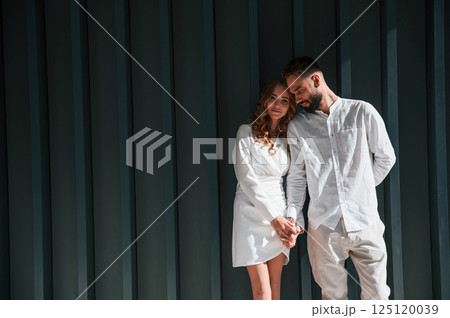 Beautiful young couple is standing together against dark green background Beautiful young couple is standing together against dark green background 125120039