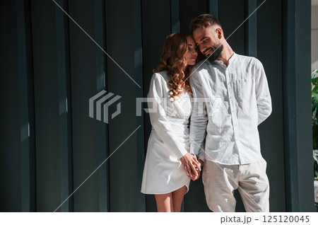 Beautiful young couple is standing together against dark green background Beautiful young couple is standing together against dark green background 125120045