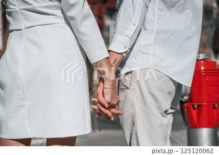Tattoos on hands. His only. Beautiful young couple is together on the street against old building 125120062