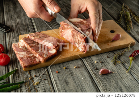 A person is skillfully cutting through gourmet meat on a wooden board, surrounded by fresh ingredients and spices, in a cozy kitchen environment during the evening A person is skillfully cutting through gourmet meat on a wooden board, surrounded by fresh ingredients and spices, in a cozy kitchen environment during the evening 125120079