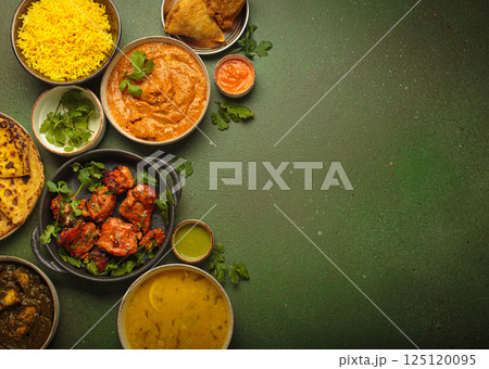 Traditional assorted Indian dishes arranged top view on green background table. Cuisine of India, space for text 125120095
