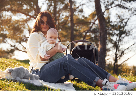 Sitting on the ground. Beautiful mother with her little son is outdoors in the forest 125120166