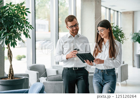 Holding tablet. Man and woman in formal clothes are working together indoors 125120264