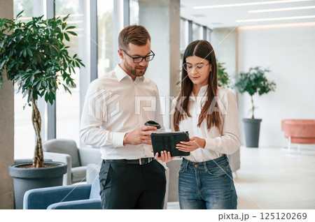 With tablet in hands. Man and woman in formal clothes are working together indoors 125120269