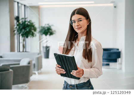 With digital tablet in hands. Young woman in glasses and in formal wear is indoors With digital tablet in hands. Young woman in glasses and in formal wear is indoors 125120349