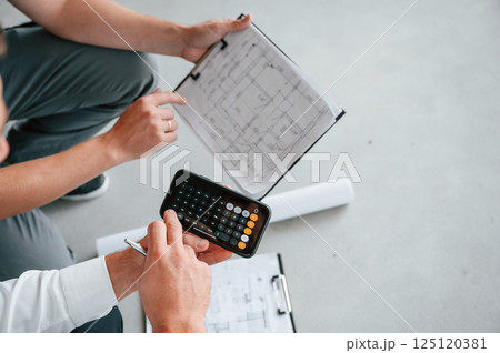Sitting, using calculator. Manager with foreman are working on the construction site together Sitting, using calculator. Manager with foreman are working on the construction site together 125120381