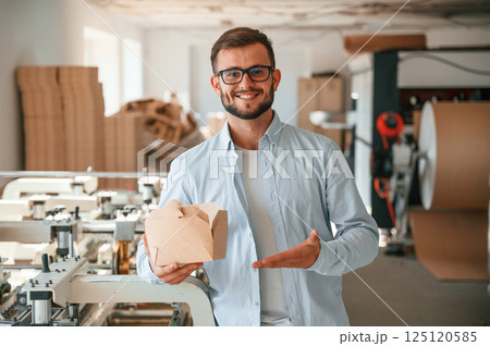 Holding and showing wooden sheets. Print house worker in white clothes is indoors 125120585