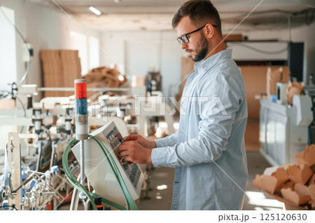 Machine operator is busy by setting up a device. Print house worker in white clothes is indoors Machine operator is busy by setting up a device. Print house worker in white clothes is indoors 125120630