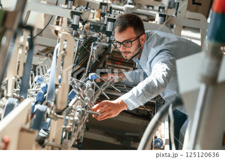 Setting up a printing machine. Typography worker in white clothes is indoors 125120636