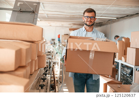Moving the boxes with raw material. Print house worker in white clothes is indoors Moving the boxes with raw material. Print house worker in white clothes is indoors 125120637