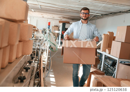 Moving the boxes with raw material. Print house worker in white clothes is indoors 125120638