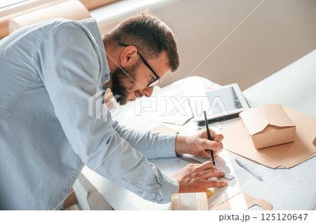 Doing measurements and drawing new design. Print house worker in white clothes is indoors Doing measurements and drawing new design. Print house worker in white clothes is indoors 125120647