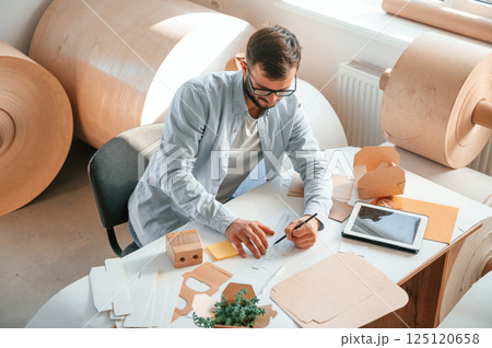 Sitting and working by the table. Print house employee in white clothes is indoors 125120658