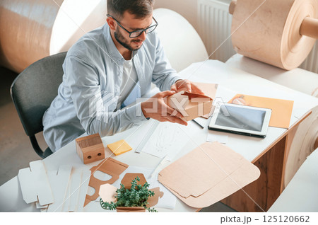 Sitting and working by the table. Print house employee in white clothes is indoors Sitting and working by the table. Print house employee in white clothes is indoors 125120662
