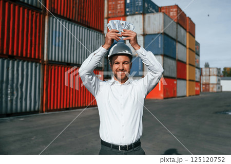 Happy man holding currency. Male worker is on the location with containers 125120752