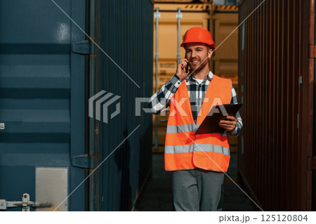 Using phone and holding tablet. Male worker is on the location with containers 125120804
