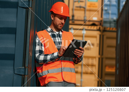 With digital tablet in hands. Male worker is on the location with containers With digital tablet in hands. Male worker is on the location with containers 125120807