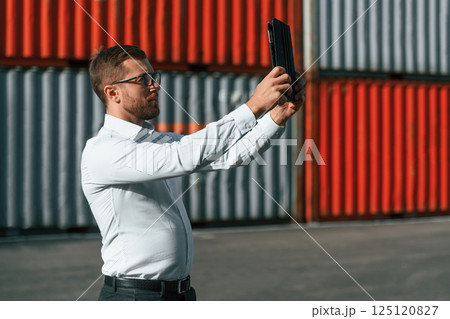 Taking photos by using tablet. Male worker is on the location with containers 125120827