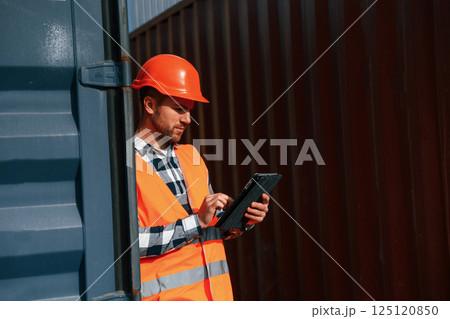 Male worker is on the location with containers. Using digital tablet 125120850