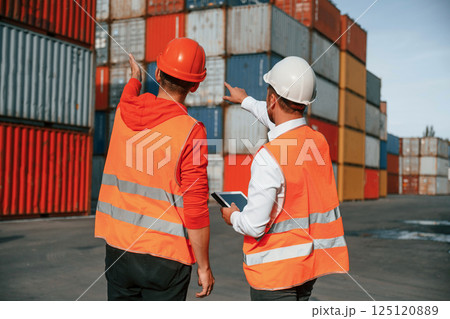 Showing the objects. Two male workers is on the location with containers 125120889
