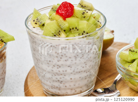 Yogurt and chia seed pudding in a glass, kiwi pieces. White table 125120990