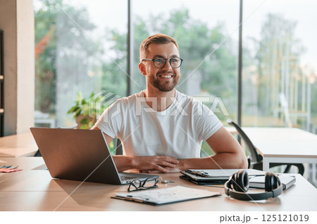 Sitting and smiling. Positive man in formal clothes is working in the modern office Sitting and smiling. Positive man in formal clothes is working in the modern office 125121019
