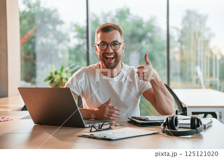 Sitting and smiling. Positive man in formal clothes is working in the modern office Sitting and smiling. Positive man in formal clothes is working in the modern office 125121020