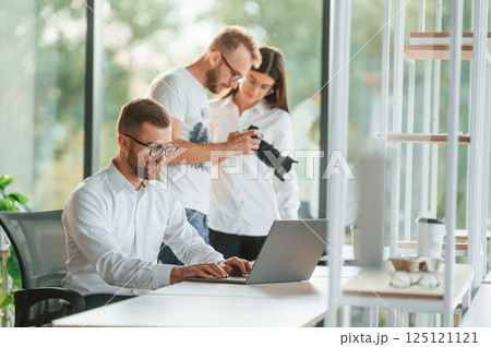Man showing photos on the camera to a woman. Three people in formal clothes are working in the modern office together 125121121