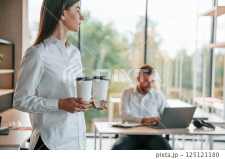 Giving drink to the boss. Man and woman are working in the modern office together Giving drink to the boss. Man and woman are working in the modern office together 125121180