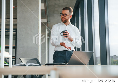 Holding cup of drink. Man in formal clothes is working in the modern office Holding cup of drink. Man in formal clothes is working in the modern office 125121213