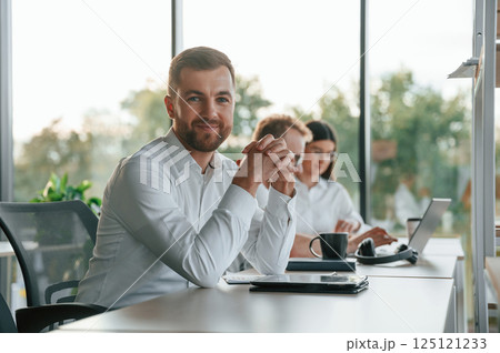 Man is looking at the camera. Three people in formal clothes are working in the modern office together 125121233