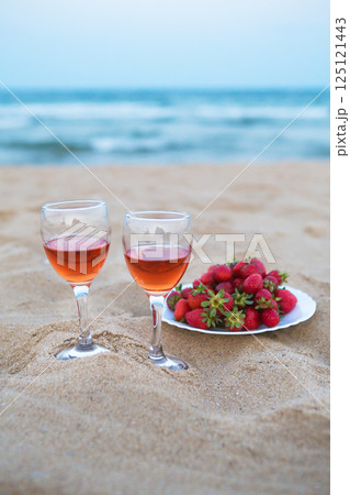 Two glasses of rose wine and a plate of fresh strawberries sit on a sandy beach, enjoying the ocean view Two glasses of rose wine and a plate of fresh strawberries sit on a sandy beach, enjoying the ocean view 125121443