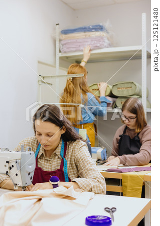 Three women seamstresses and fashion designers work in for sewing machines, clothing production. Three women seamstresses and fashion designers work in for sewing machines, clothing production. 125121480