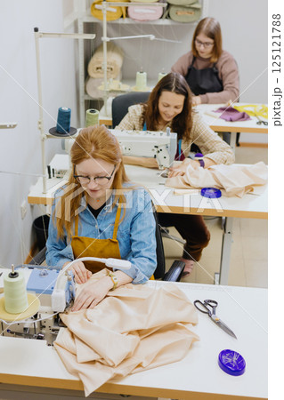 Three women seamstresses and fashion designers work in for sewing machines, clothing production. Three women seamstresses and fashion designers work in for sewing machines, clothing production. 125121788
