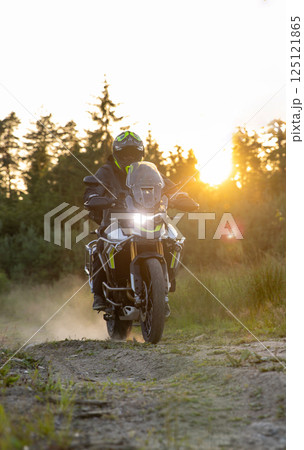 Driver riding motorcycle on gravel road during sunset, spring mountains Driver riding motorcycle on gravel road during sunset, spring mountains 125121865